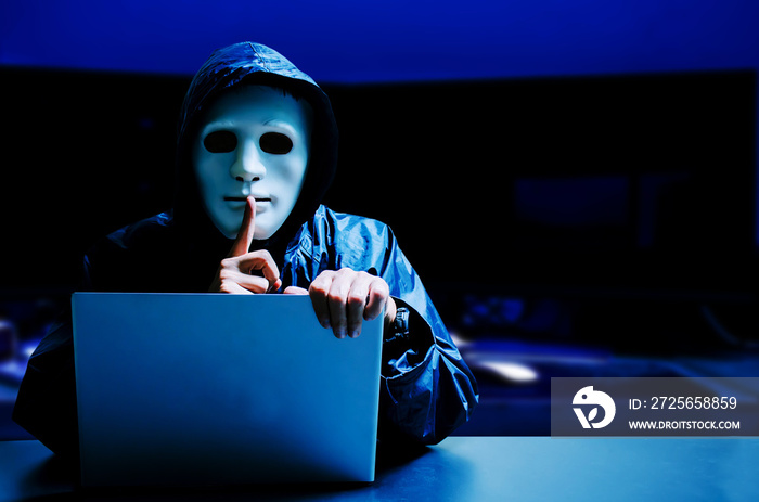 Anonymous computer hacker in white mask and hoodie. Obscured dark face making silence gesture in Und