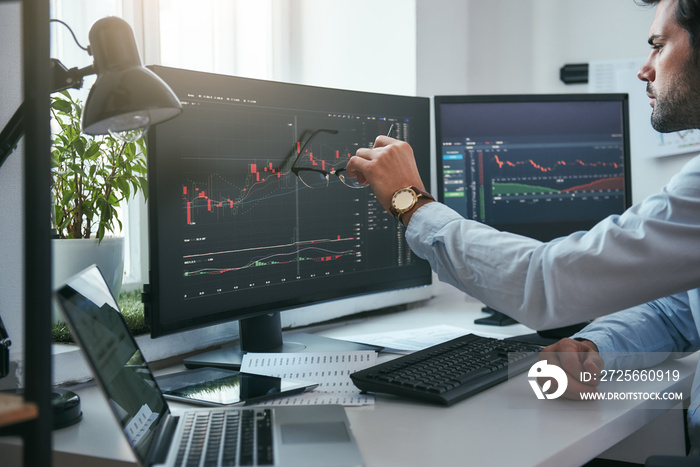 Forex market. Young trader is pointing at graphs on computer screen and analyzing data while working