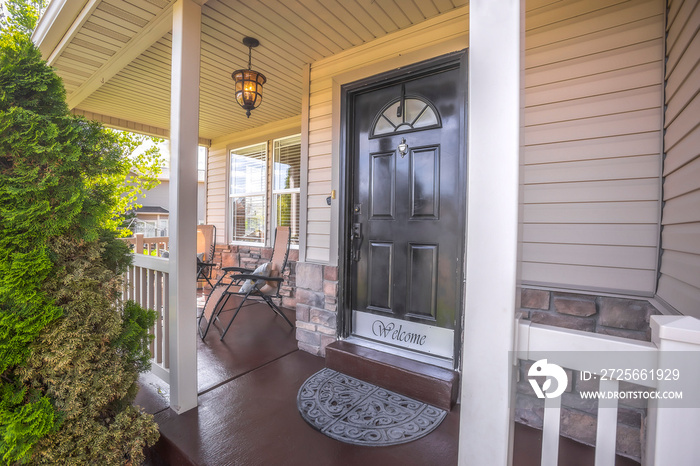 Home with chairs on porch and brown door with glass panes and welcome sign