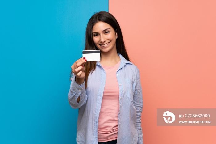 Young woman over pink and blue wall holding a credit card