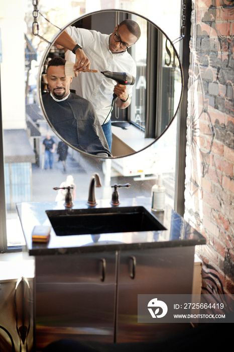 Barber cutting mans hair seen through mirror