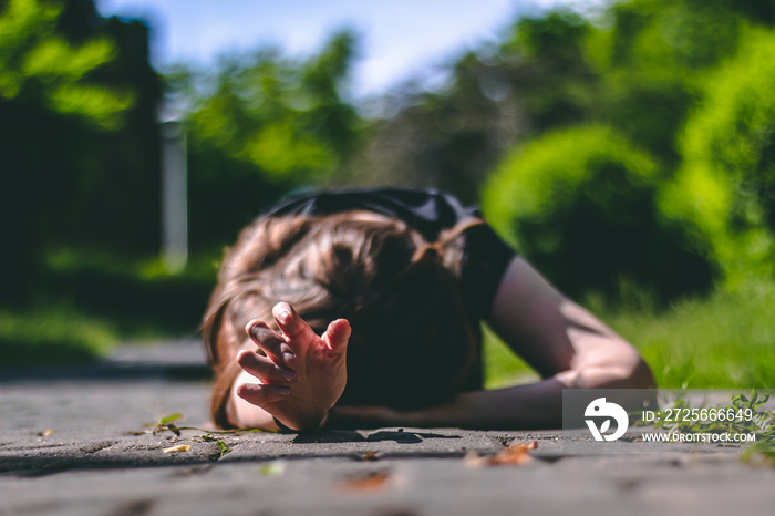 Young woman with brown hair wearing a black t-shirt lying on an alley in the park with one hand reac