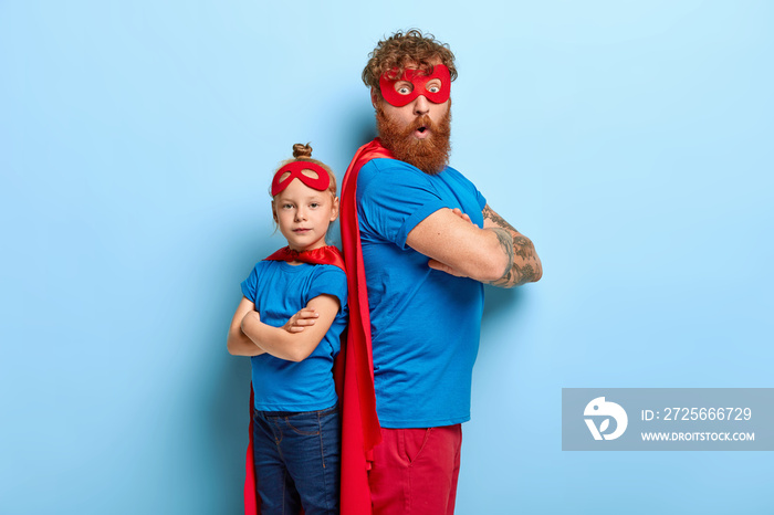 红发父女一起玩超级英雄游戏，背靠背，玩得开心，穿蓝色和红色