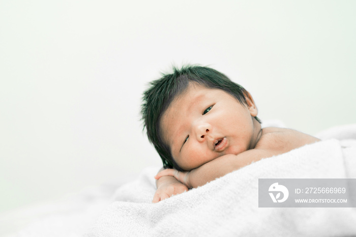 Happy cute adorable Asian baby boy with black hair lying a white blanket.