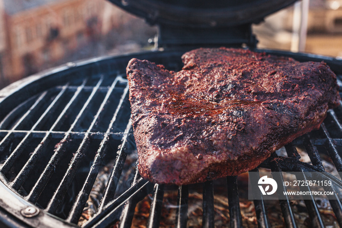 Close up on the blackened and charred bark of a smoked beef brisket, in a slow cooking background