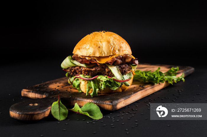 Tasty craft burger with grilled meat, cheese, tomato on the black background