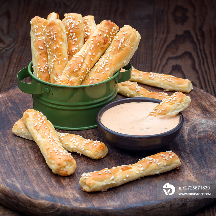 Homemade savory bread sticks with cheese and sesame in a basket, served with sauce on wooden board, 