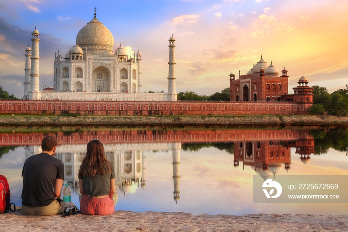 Taj Mahal Agra at sunset with moody sky and water reflection enjoyed by tourist couple sitting at Me