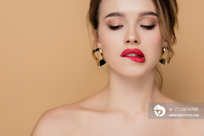 sensual woman with makeup and bare shoulders biting lip isolated on beige.