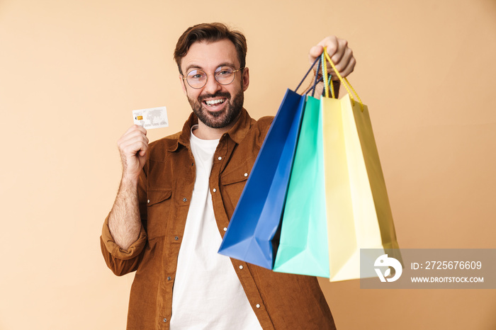 Cheery young man holding credit card and shopping bags.