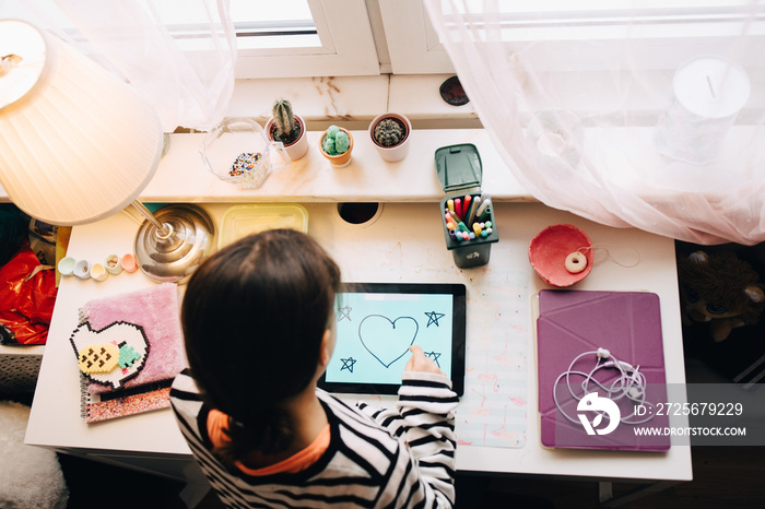 High angle view of little girl drawing on digital tablet at table in bedroom