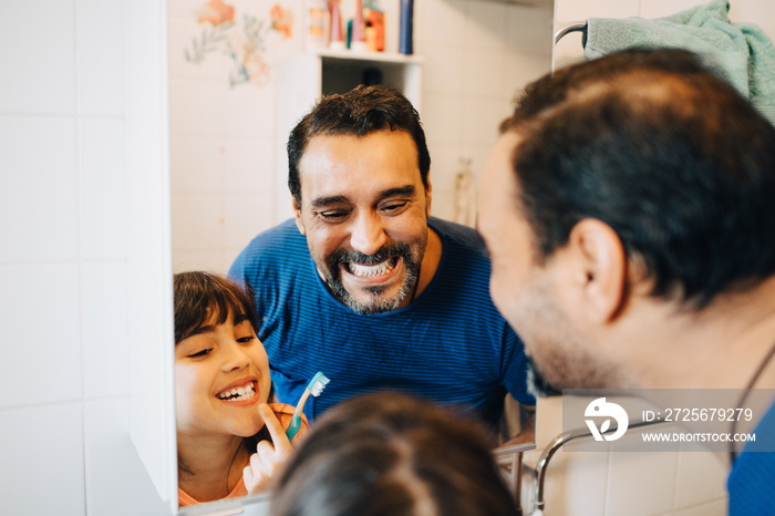 Father and daughter looking at teeth in mirror while brushing in bathroom