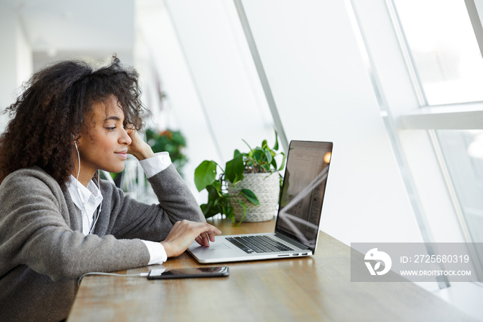 Portrait of young woman using laptop and cellphone while sitting by window