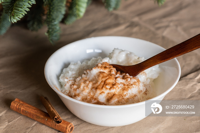 Traditional Scandinavian rice porridge and cinnamon sticks. Rice pudding is in a white plate on craf