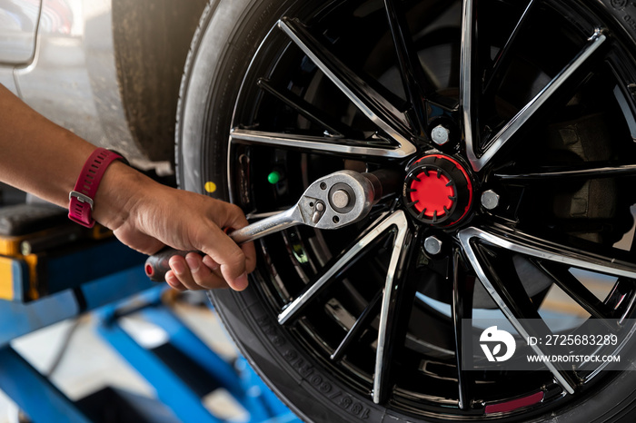 Car service, repair and maintenance concept - auto mechanic man changing tire in auto repair shop.