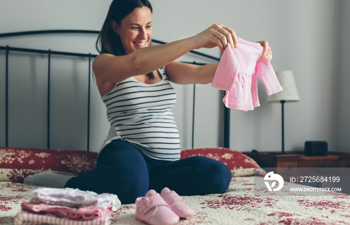 孕妇看起来像女婴的衣服和鞋子。选择性关注婴儿开衫