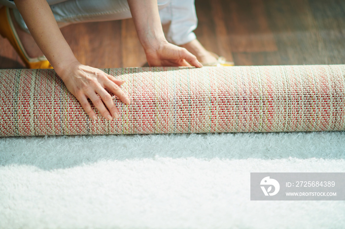 woman at home in sunny day folding carpet into roll