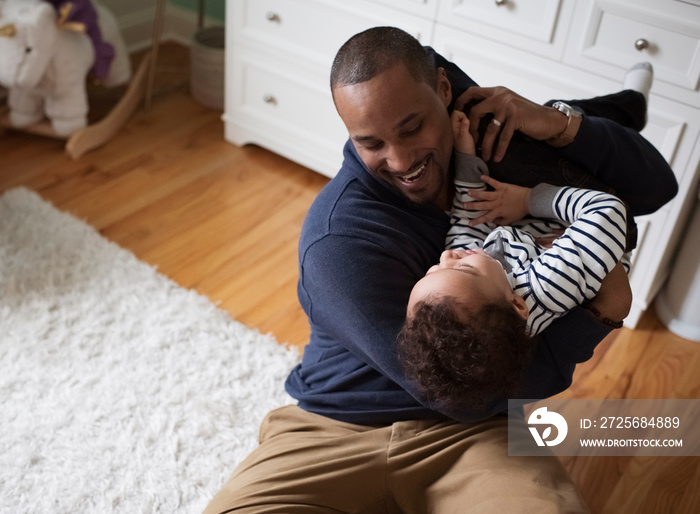 High angle view of playful father carrying happy son while sitting on rug at home