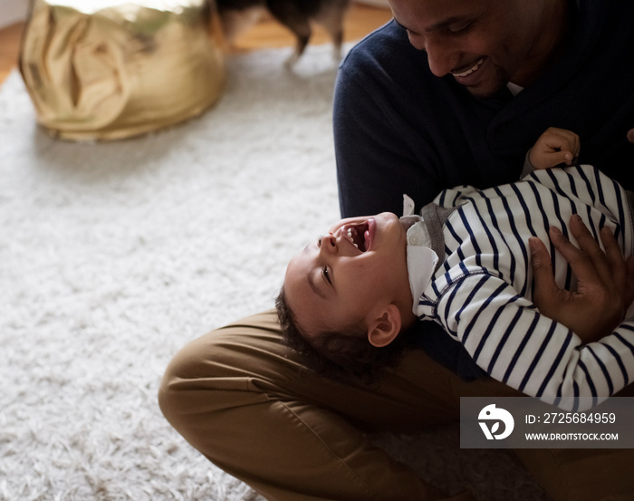 Father carrying happy son while sitting on rug at home