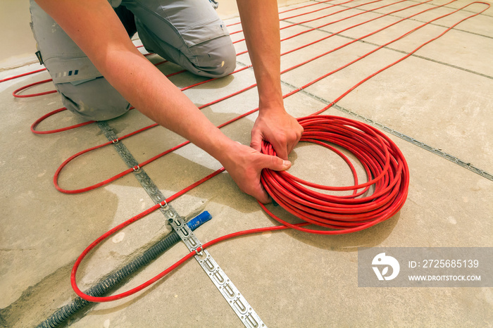 Electrician installing heating red electrical cable wire on cement floor in unfinished room. Renovat