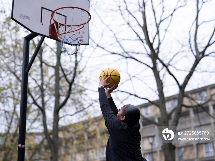 Teenage girl playing basketball outdoors