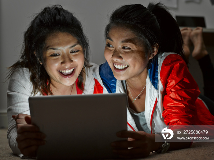 Two young women lying on floor looking at digital tablet