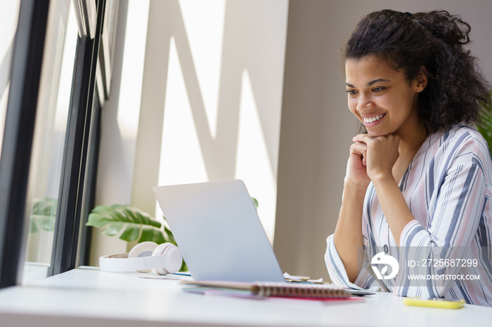 Beautiful smiling African American woman freelancer looking at digital screen working from home. Hap