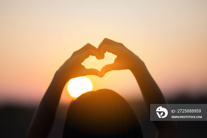 hands forming a heart shape with sunset silhouette