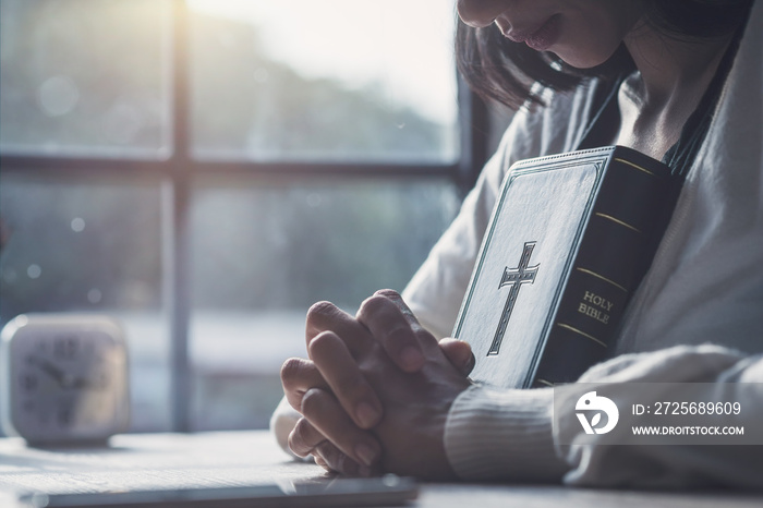 Christian girl holding hands with Bible to pray for blessings from God by faith.