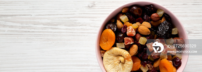 Dried fruits and nuts in a pink bowl over white wooden background, overhead view. Top view, from abo