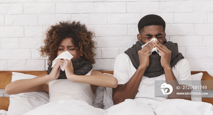 Sick african-american couple blowing noses in bed