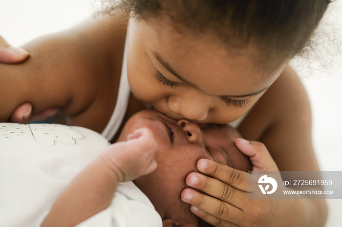 african american sister child kissing her newborn baby brother with love