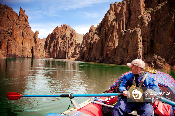 Boatman looking over shoulder while paddling inflatable boat along river