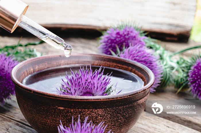 Thistle oil and thistle flowers on wooden background.