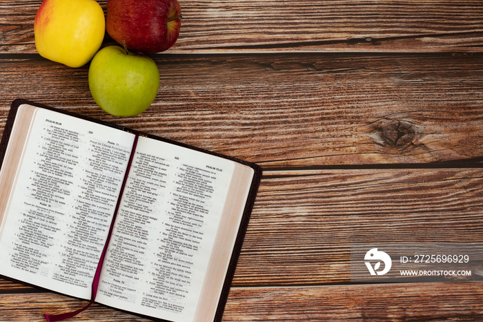 圣经书，三个不同颜色的苹果被隔离在木桌背景上。复制空间