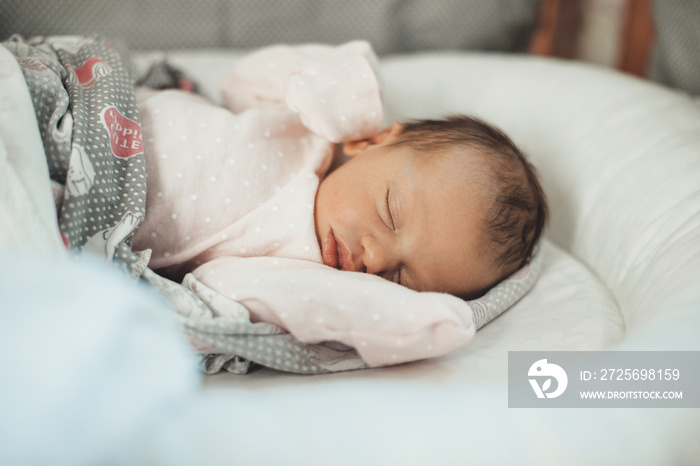 Close up photo of a sleeping newborn baby in warm clothes covered with a quilt in her bed