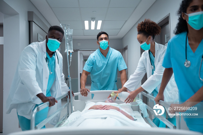 Mixed race doctors wearing face masks transporting patient in hospital bed