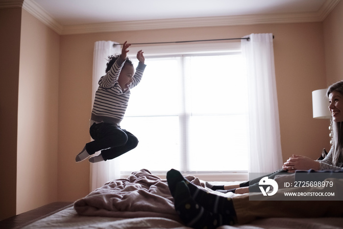 Mother looking at son jumping on bed while sitting with father in bedroom