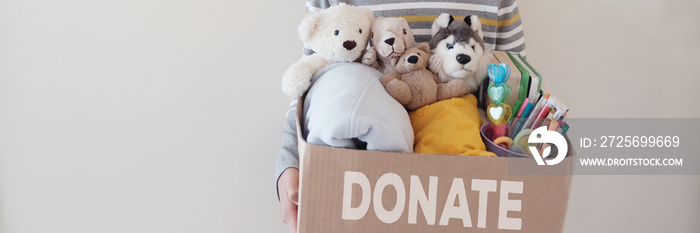 Young volunteer preteen teenage boy holding a box full of used toys, cloths, books and stationery fo