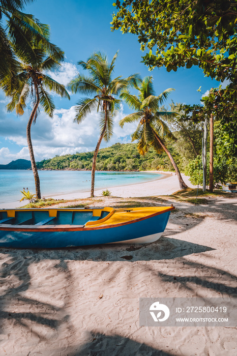 Mahe island, Seychelles. Local vivid colored boat under coconut palm trees on sunny day on shore of 