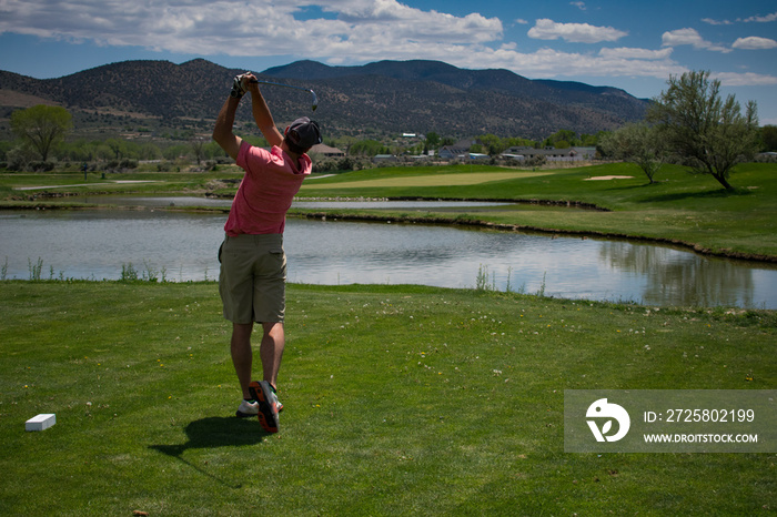 Young Male Golfer Hitting a Golf Ball Off of the Tee Box - Mountains in the background