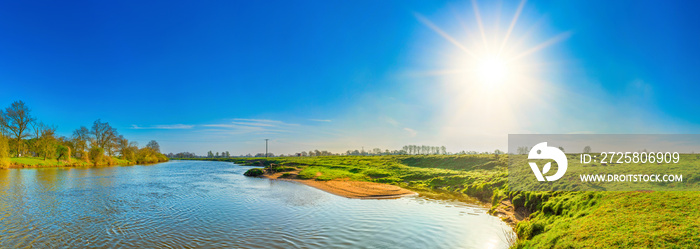 Landschaft im Frühling mit Bäumen, Wiesen, Fluss und Sonne