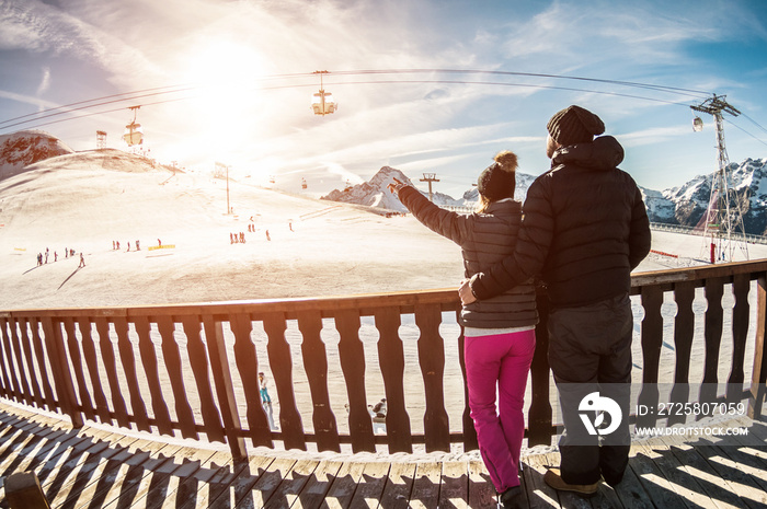 Young couple in winter vacation at snow resort mountain - Skiers tourists relaxing in ski slope chal