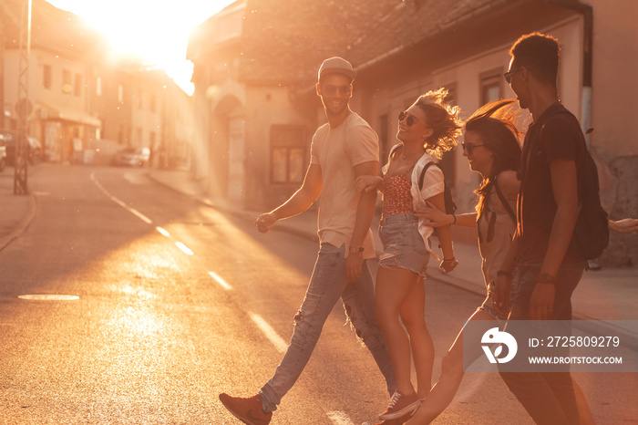 Group of friends walking and laughing at the city street at sunset.