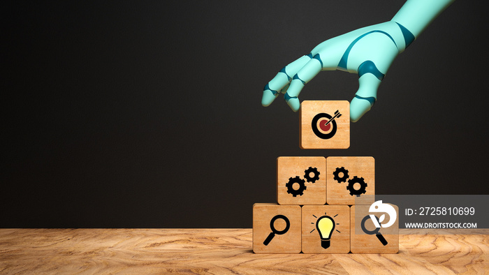 robot hand adding a cube with a target symbol to a stack of cubes on wooden base in front of a black