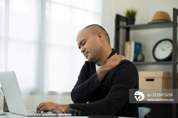 Business Asian man in suit sitting in home working with laptop he has shoulder neck pain and hurt ge