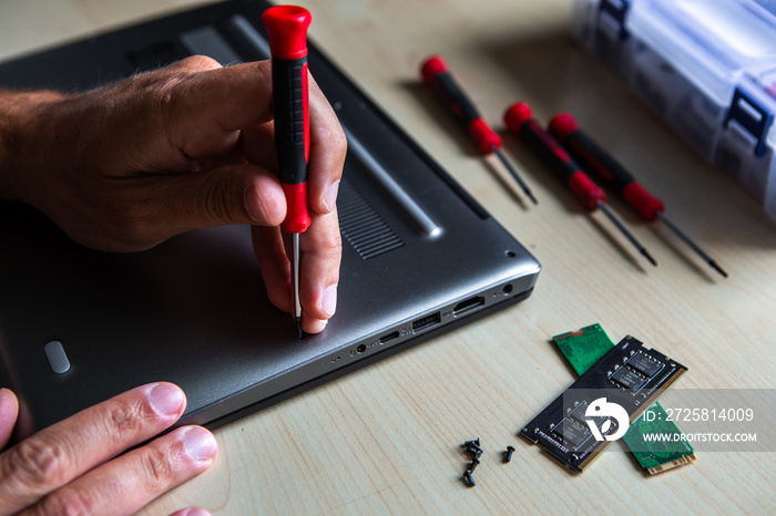 The hand of a young serviceman man opening a laptop computer with a red screwdriver. the laptop is o
