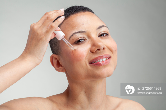 Portrait�of smiling woman applying serum on cheek