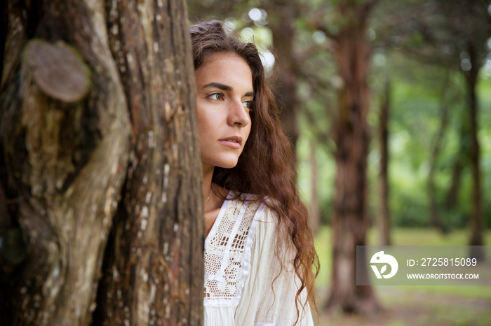 Young woman standing behind tree trunk