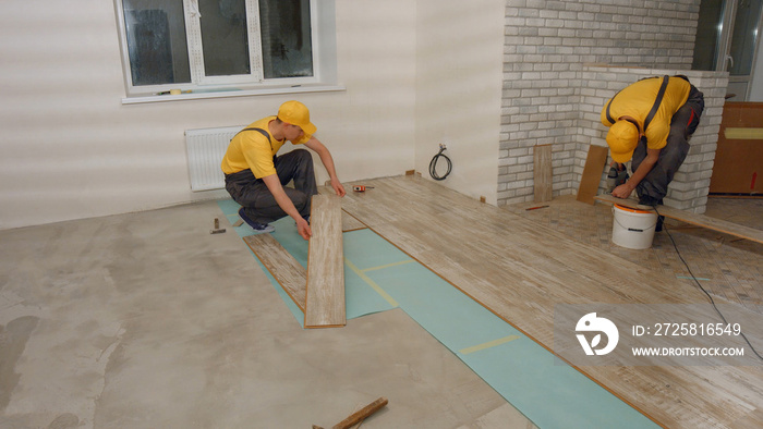 Builders laying wooden laminate boards on floor. Handyman drills board in a new house. Home renovati